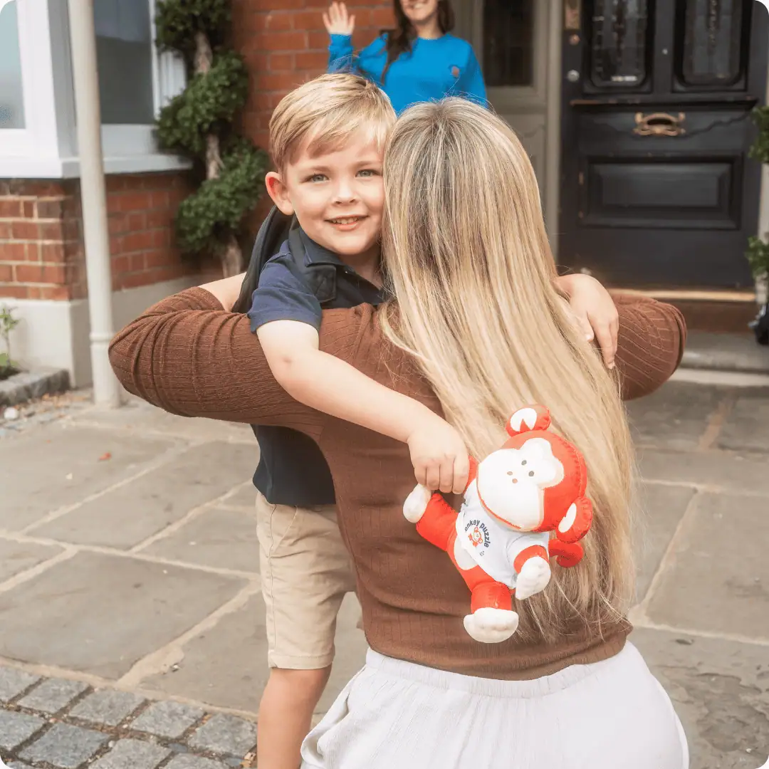 Smiling child being hugged by a woman outside Monkey Puzzle Day Nursery.