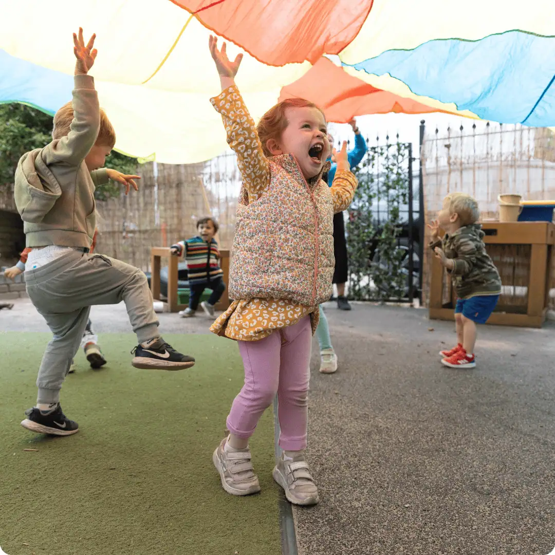 Children enjoying outdoor play under a colorful parachute at Monkey Puzzle Day Nursery.